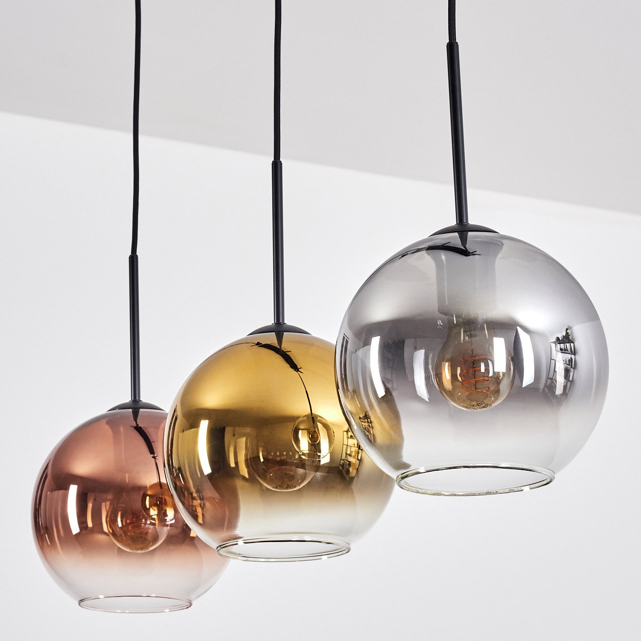 Drei kugelförmige Pendelleuchten hängen von der Decke. Sie haben verschiedene Farben: Kupfer, Gold und Silber. Jede hat eine sichtbare Glühbirne.
