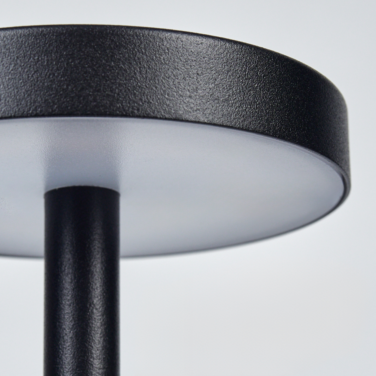 Nahaufnahme einer schwarzen Lampe. Sie hat eine runde Oberseite und einen zylindrischen Sockel. Der Hintergrund ist weiß.