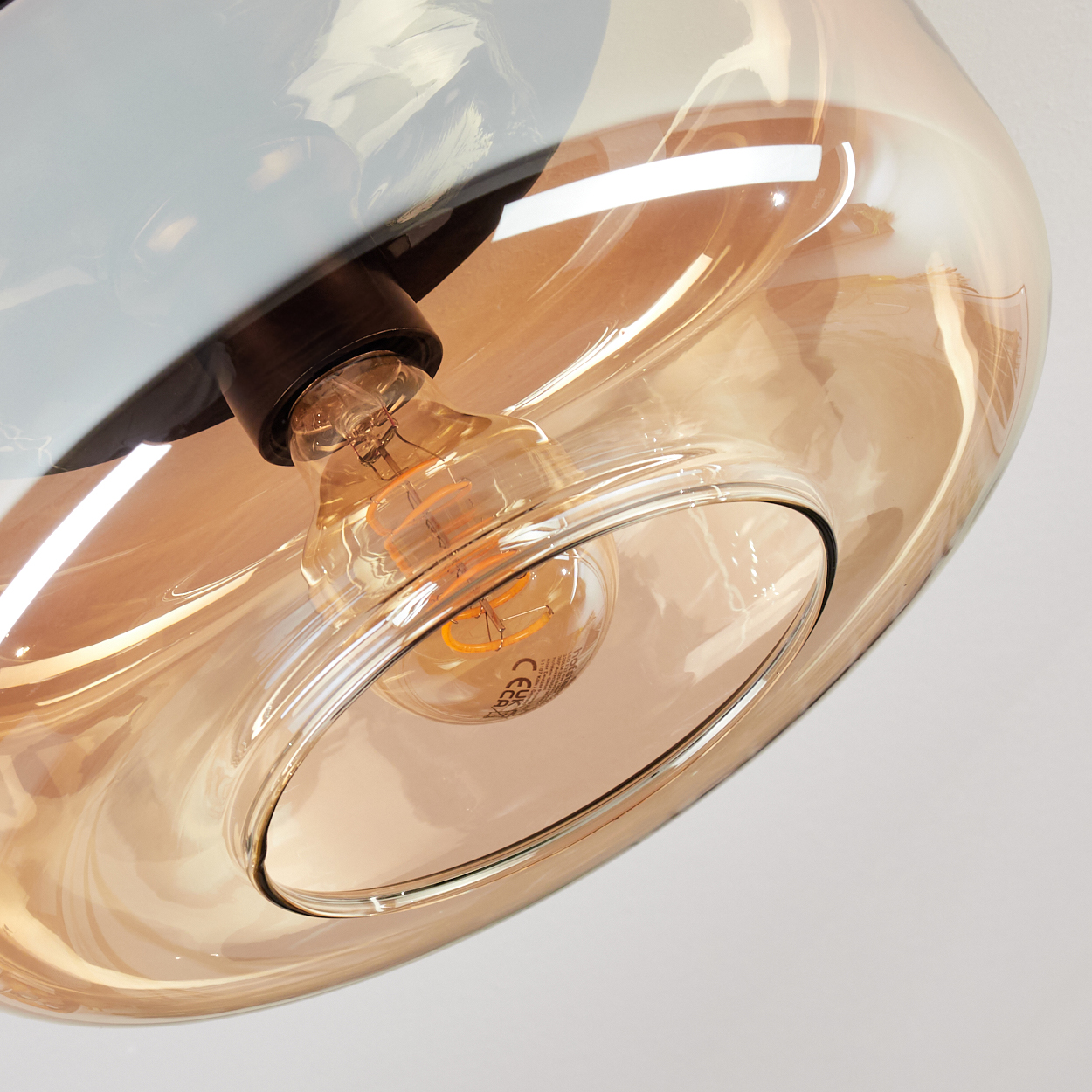Nahaufnahme einer Pendelleuchte mit tropfenförmigem, bernsteinfarbenem Glasschirm und sichtbarer Glühbirne.
