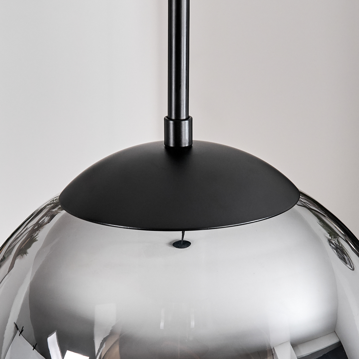 Eine moderne Pendelleuchte mit schwarzem Metallaufsatz und transparentem, kugelförmigem Glasschirm. Der Hintergrund ist eine schlichte Wand.