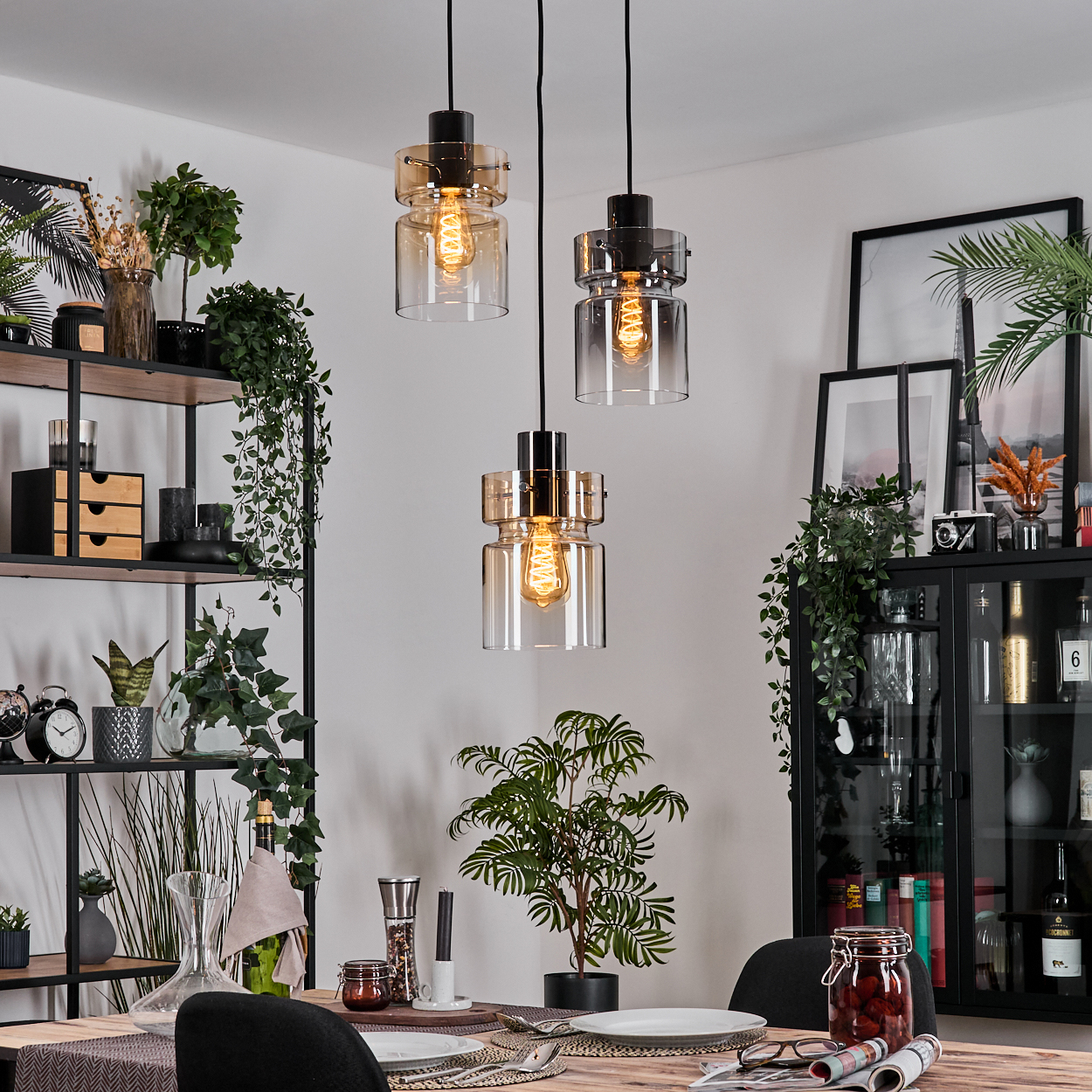 Esszimmer mit drei Hängelampen, einem gedeckten Tisch, einer Pflanze, Regalen mit Dekoration und einem Schrank.