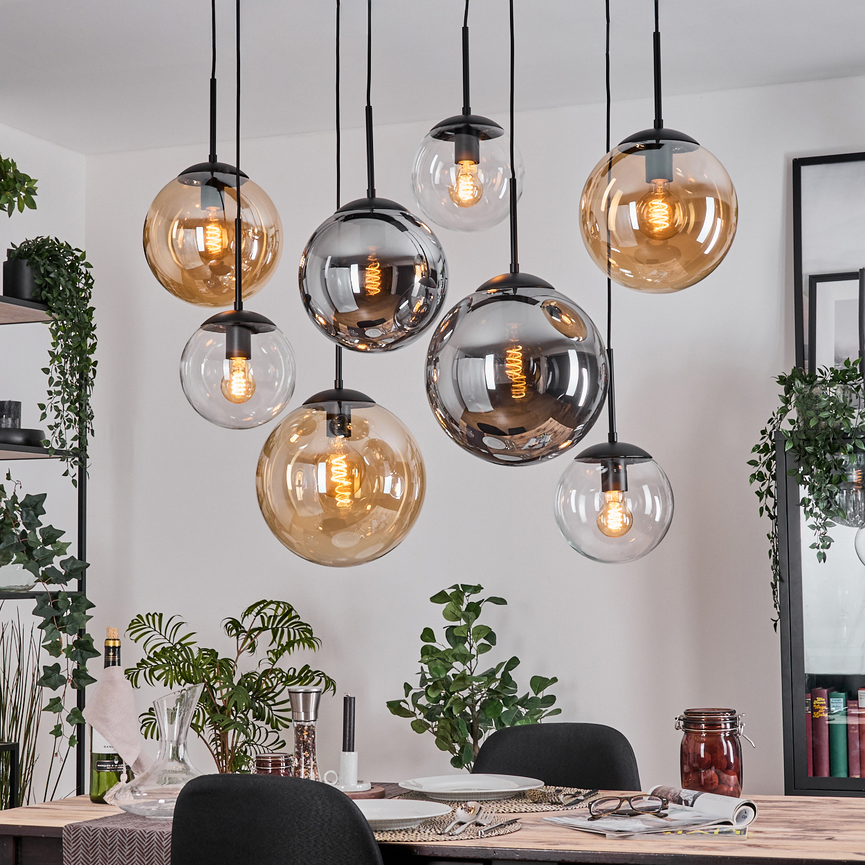 Esszimmer mit hängenden Kugelleuchten, Tisch mit Tellern und Pflanzen. Mehrere Lichter sind golden.