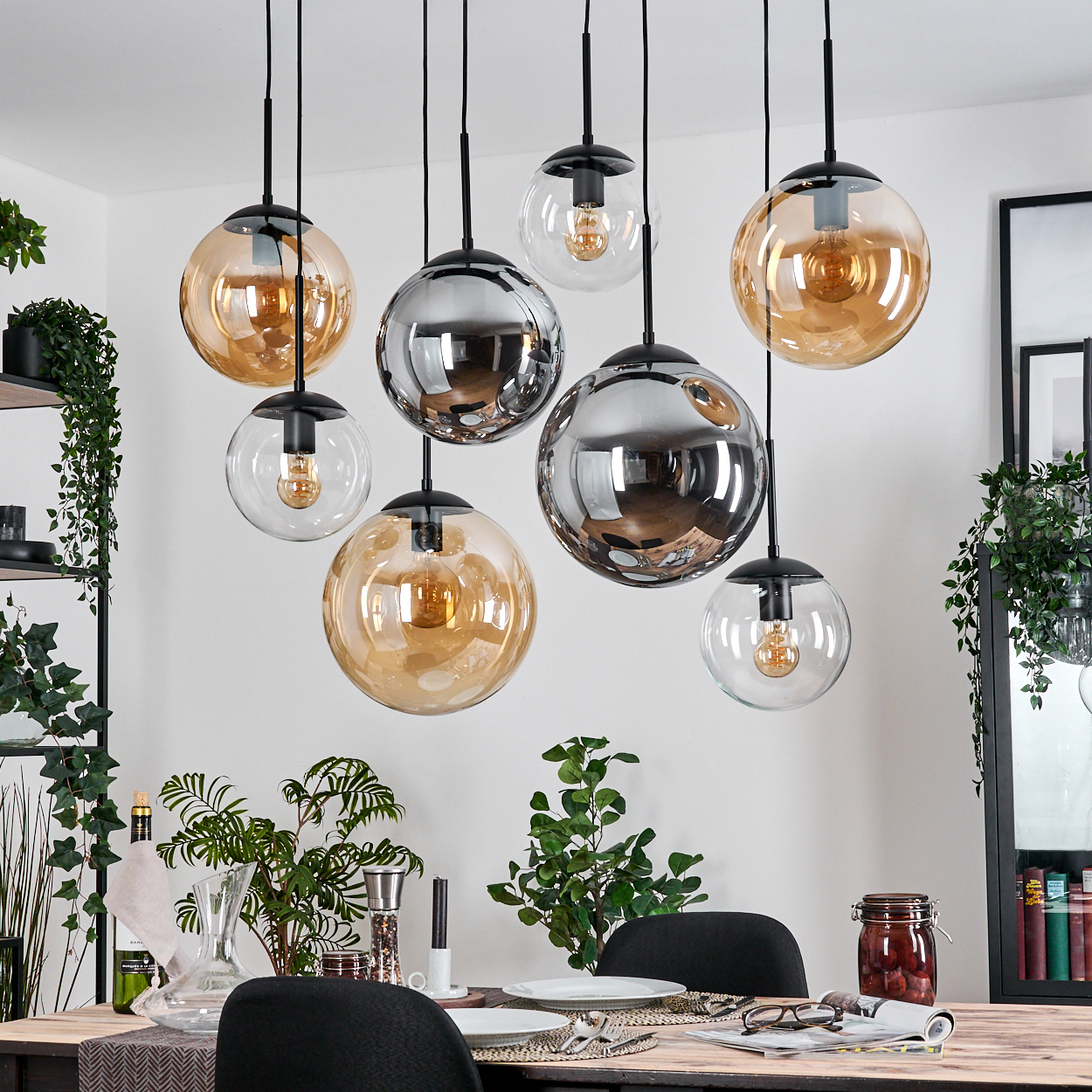 Esszimmer mit kugelförmigen Pendelleuchten. Tisch mit Pflanzen und Dekor. Hintergrund mit Regalen und einem gerahmten Bild.