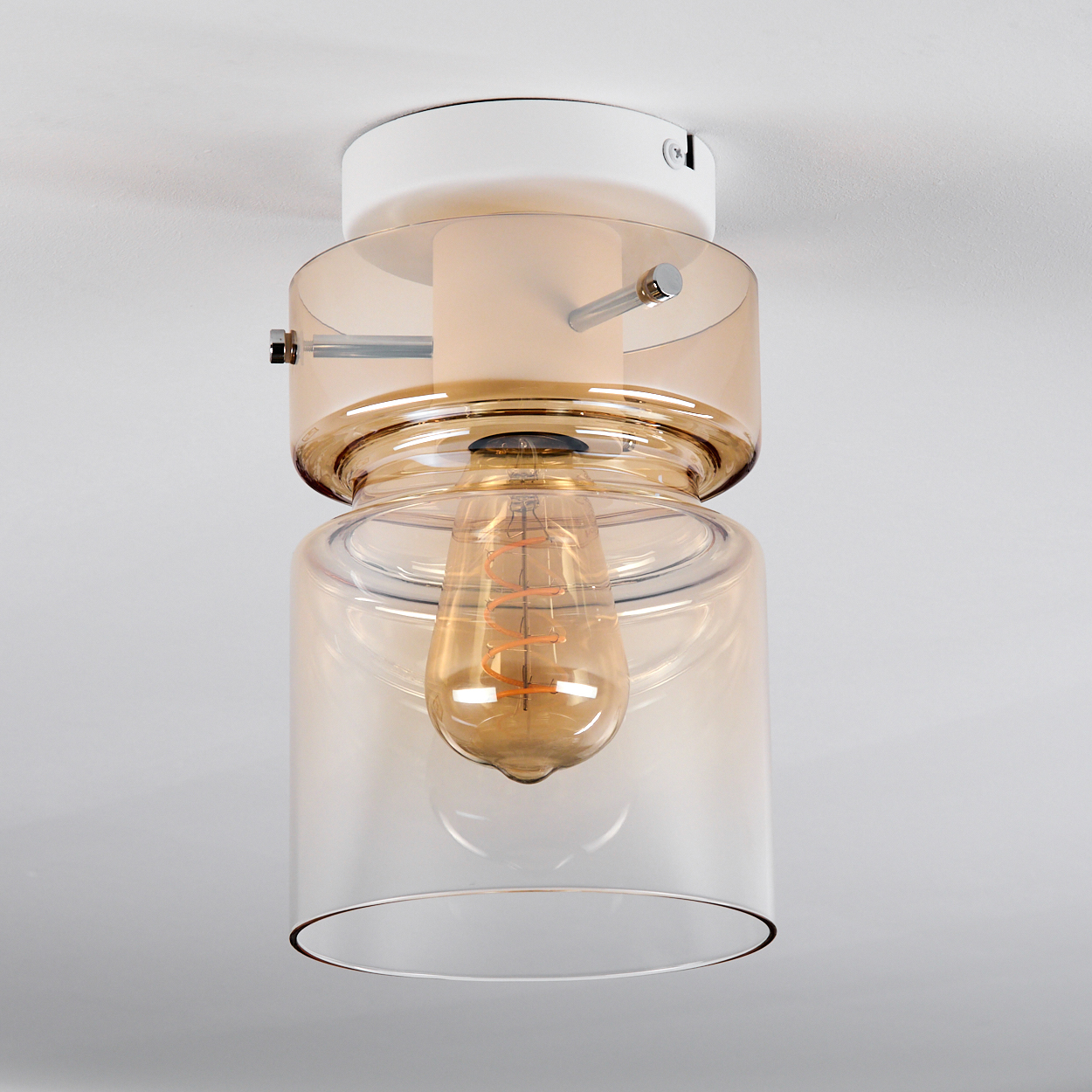 Eine moderne Deckenleuchte mit klarem Glasschirm und einer warm getönten Edison-Glühbirne. Sie ist an einer weißen Decke montiert.