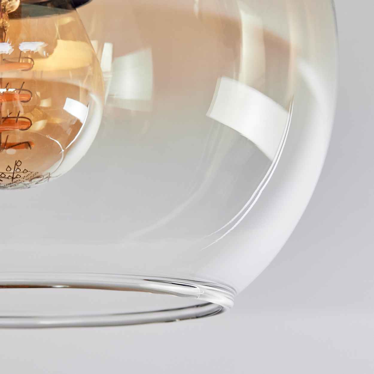 Nahaufnahme einer Glühbirne in einem Glasschirm. Die Glühbirne hat einen warmen, goldenen Schein. Der Glasschirm ist klar.