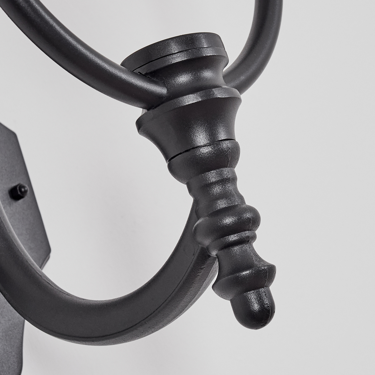 Nahaufnahme einer schwarzen, an der Wand befestigten Metall-Wandleuchte mit dekorativen Details, auf weißem Hintergrund.