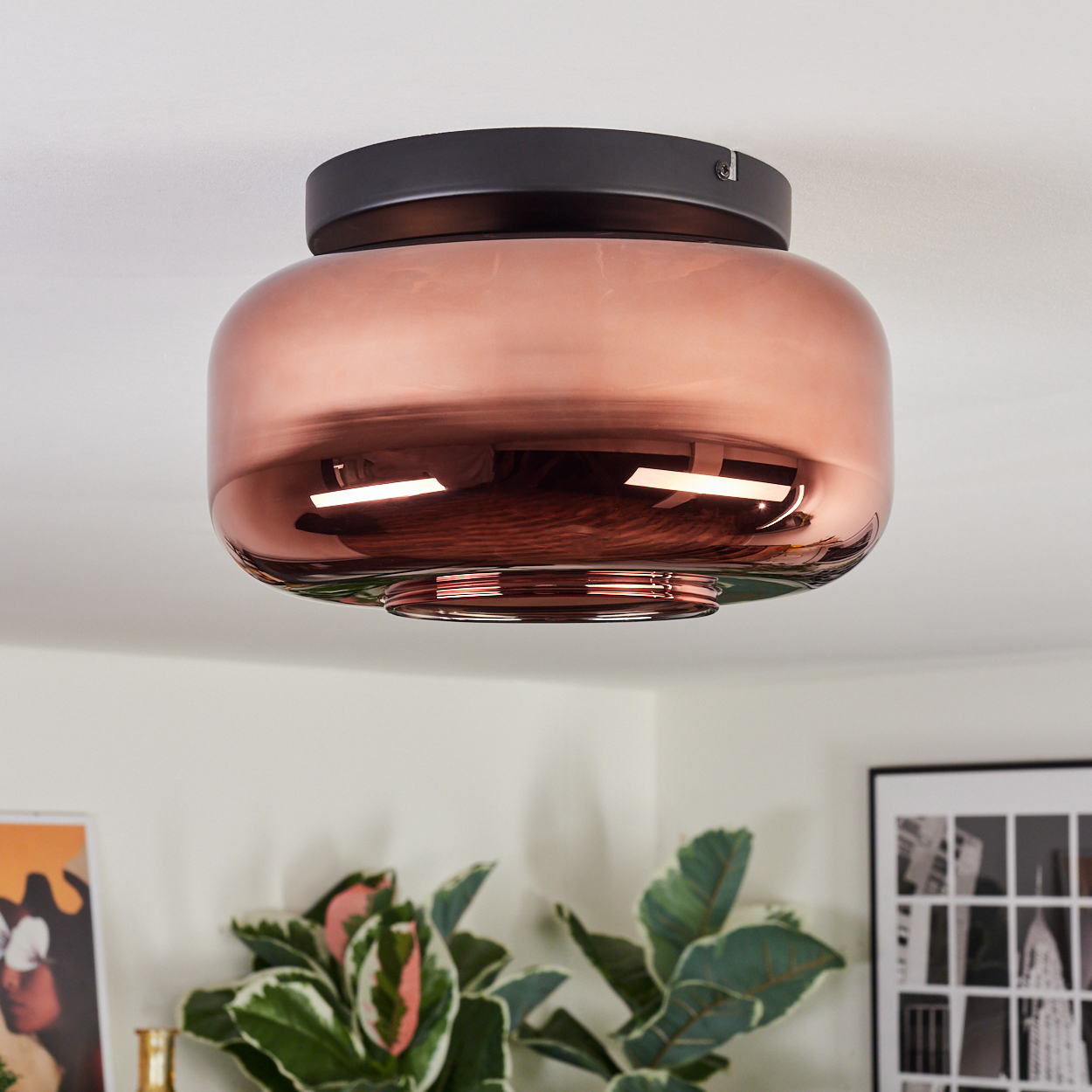 Eine moderne Deckenlampe mit kupferfarbenem Glasschirm und schwarzem Sockel. Das Licht reflektiert sich an der Decke.