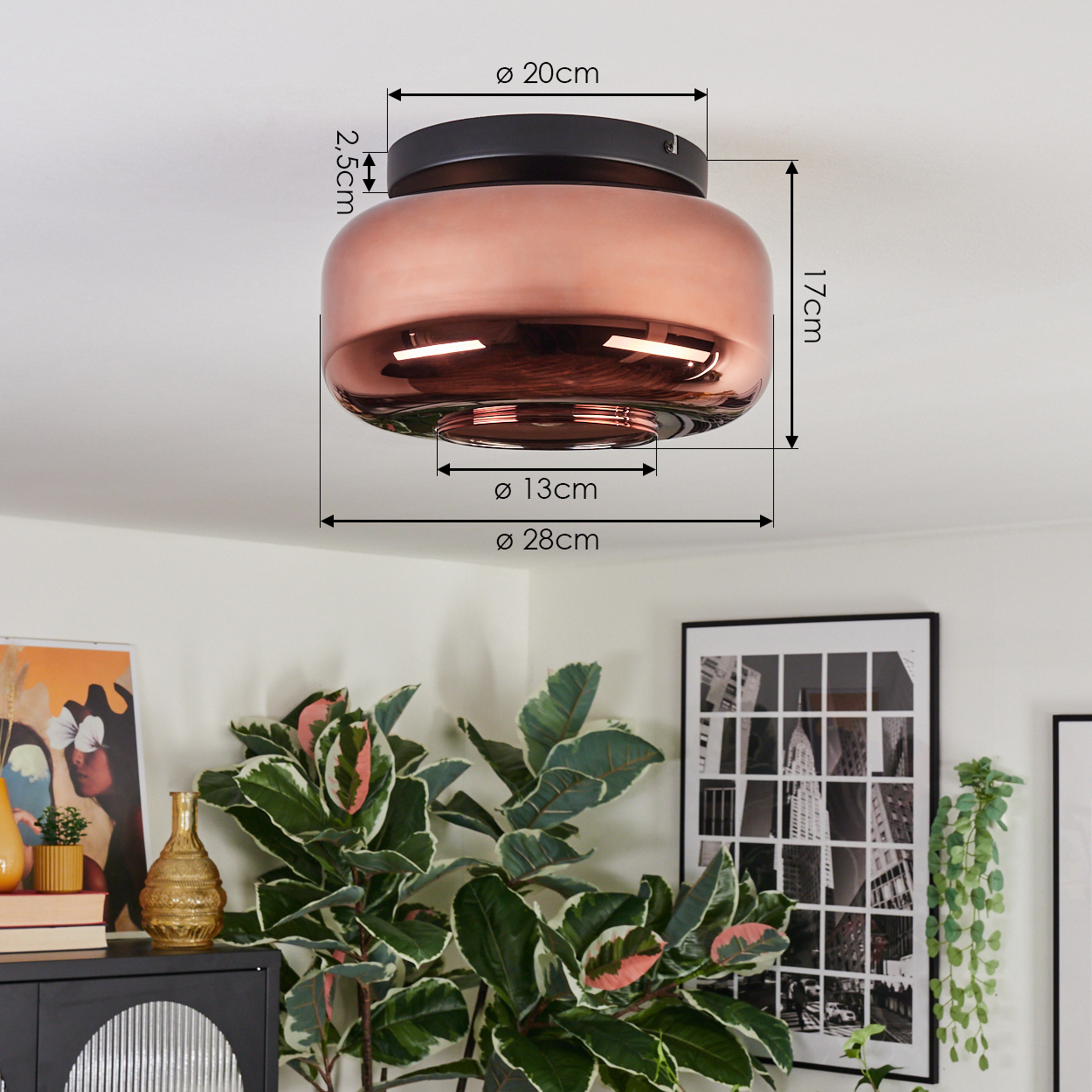 Eine kupferfarbene Deckenlampe mit markierten Abmessungen. Darunter sind ein Schrank, Pflanzen und gerahmte Kunstwerke zu sehen. Die Szene ist hell.