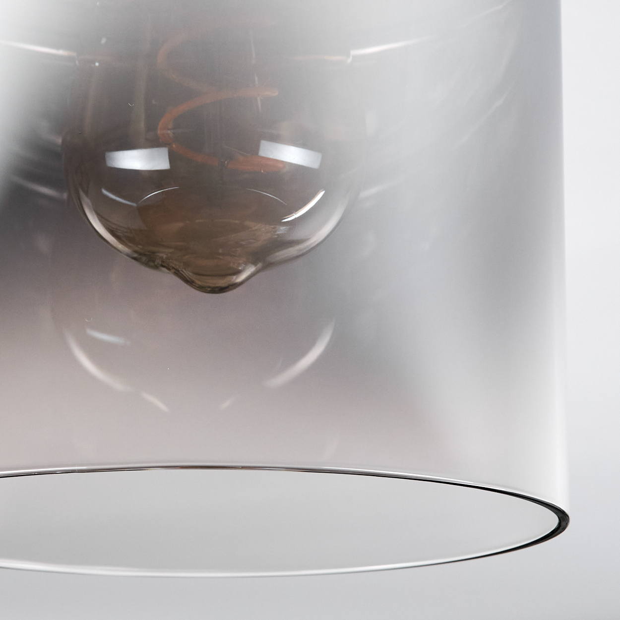 Nahaufnahme einer Lampe. Ein klarer Glasschirm umgibt eine Glühbirne mit sichtbarem Glühfaden. Der Hintergrund ist weiß und unscharf.