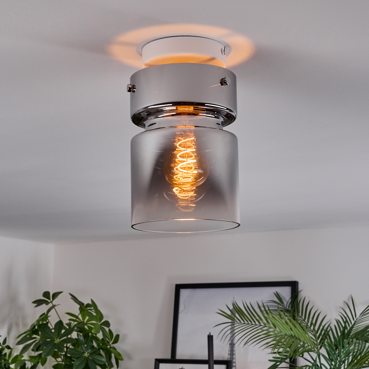 Eine moderne Deckenleuchte mit einer Wendelglühbirne hängt. Das Licht ist chromfarben und in einem rauchigen Glaszylinder eingeschlossen.