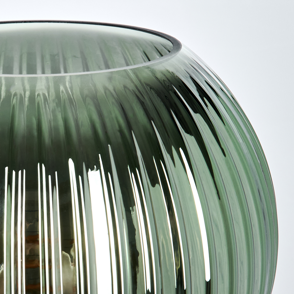 Nahaufnahme einer grünen, geriffelten Glasvase mit runder Form, vor weißem Hintergrund. Das Licht reflektiert sich im Glas.