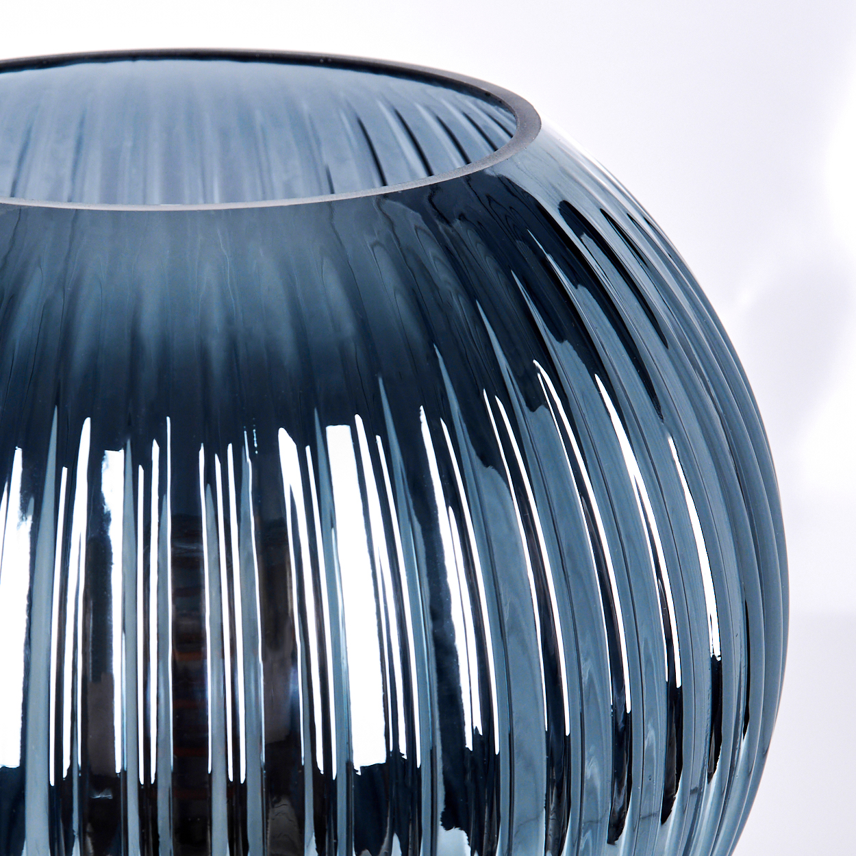 Nahaufnahme einer blauen Glasvase mit vertikalen Rippen. Die Vase hat eine weite Öffnung und steht vor weißem Hintergrund.