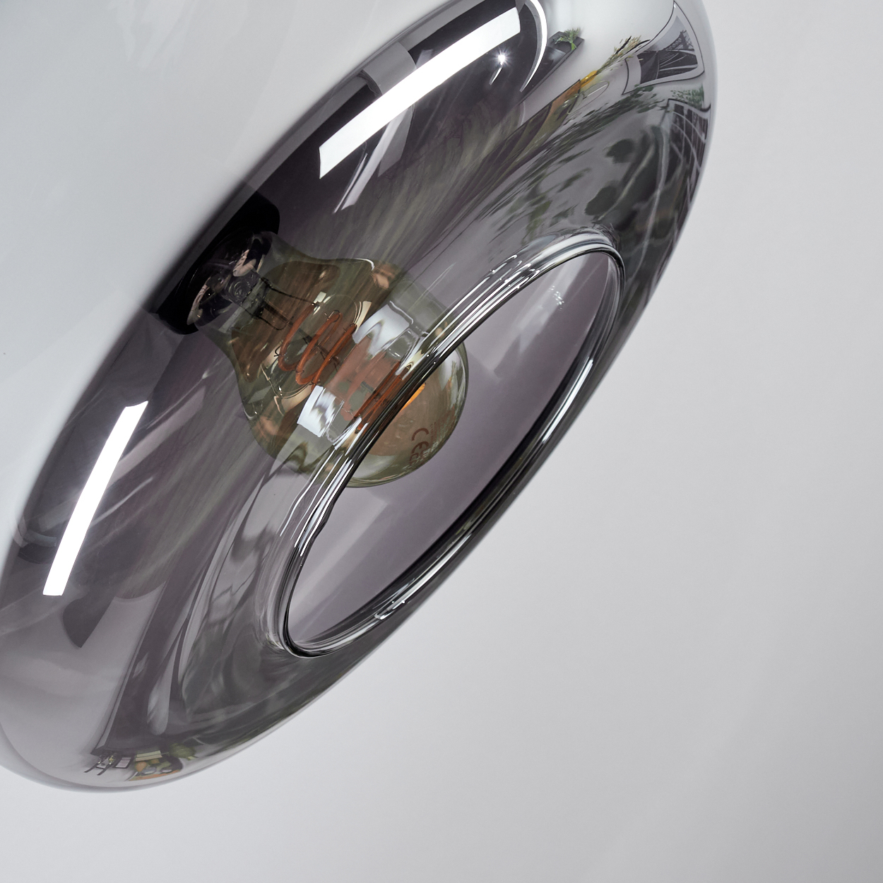 Nahaufnahme einer modernen Leuchte. Ein grauer Glasschirm umgibt eine Glühbirne, reflektiertes Licht auf weißem Hintergrund.