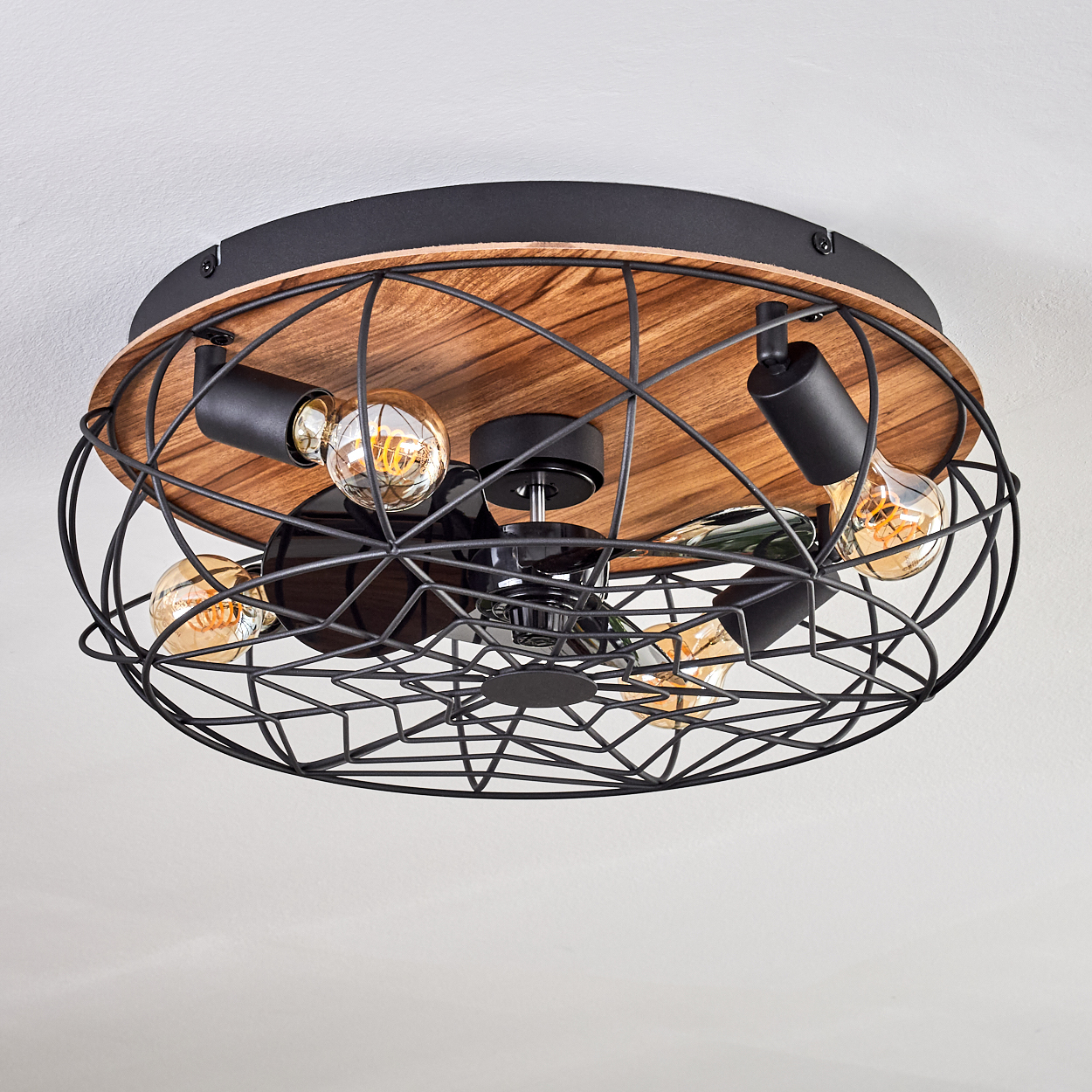 Deckenleuchte mit Edison-Glühbirnen. Schwarzer Metallkäfig und Holzsockel vor weißer Decke.