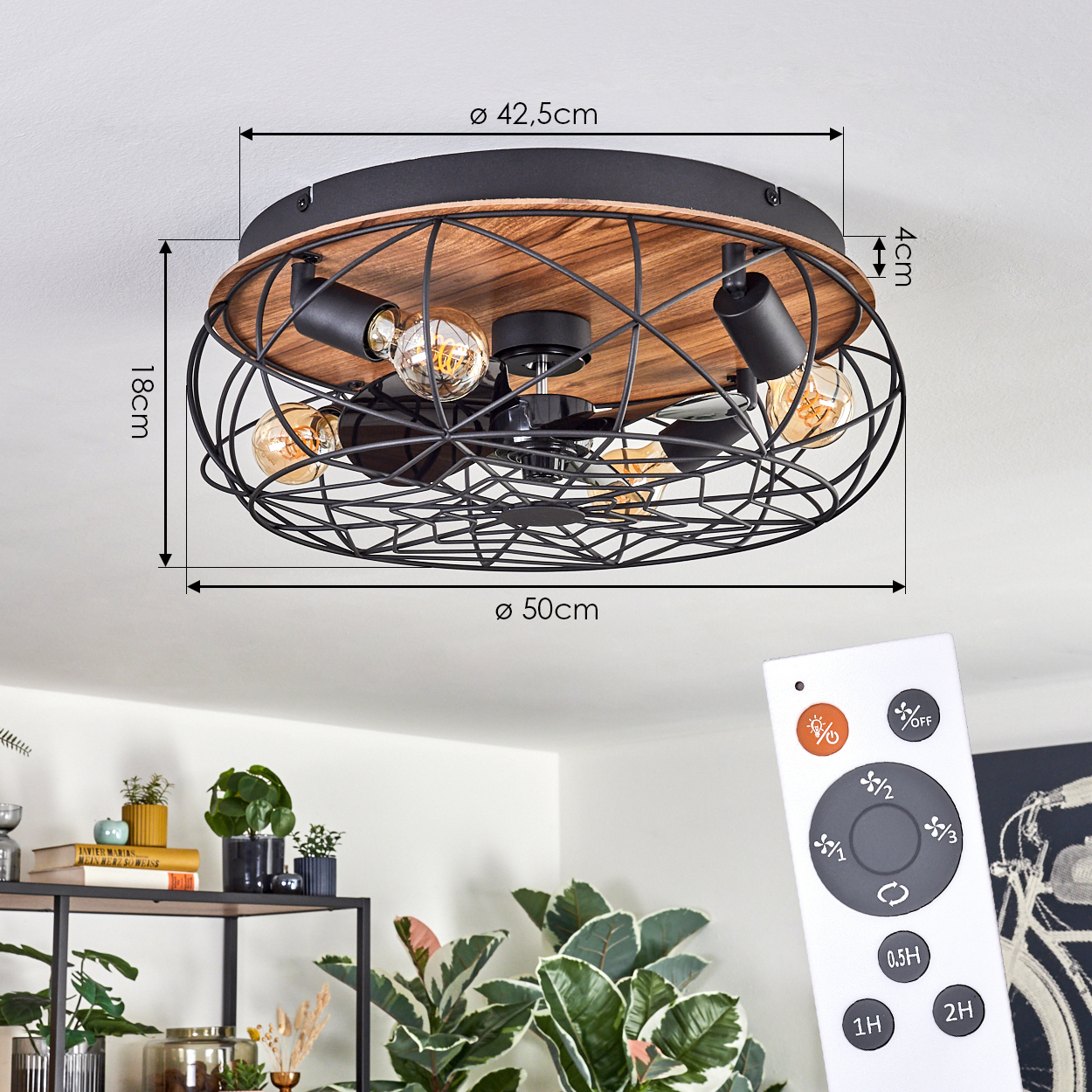Eine Deckenlampe mit schwarzem Käfigdesign, Holzsockel und sichtbaren Glühbirnen. Eine Fernbedienung im Vordergrund, Pflanzen im Hintergrund.