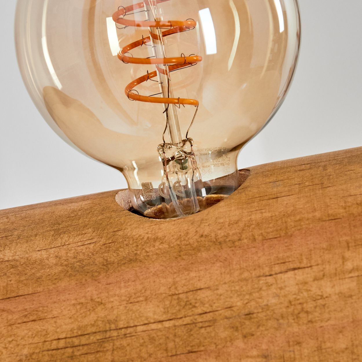 Nahaufnahme einer Glühbirne mit braunem Holzsockel. Die Birne ist aus Glas mit einem orangefarbenen, spiralförmigen Glühfaden. Der Sockel ist strukturiertes Holz.