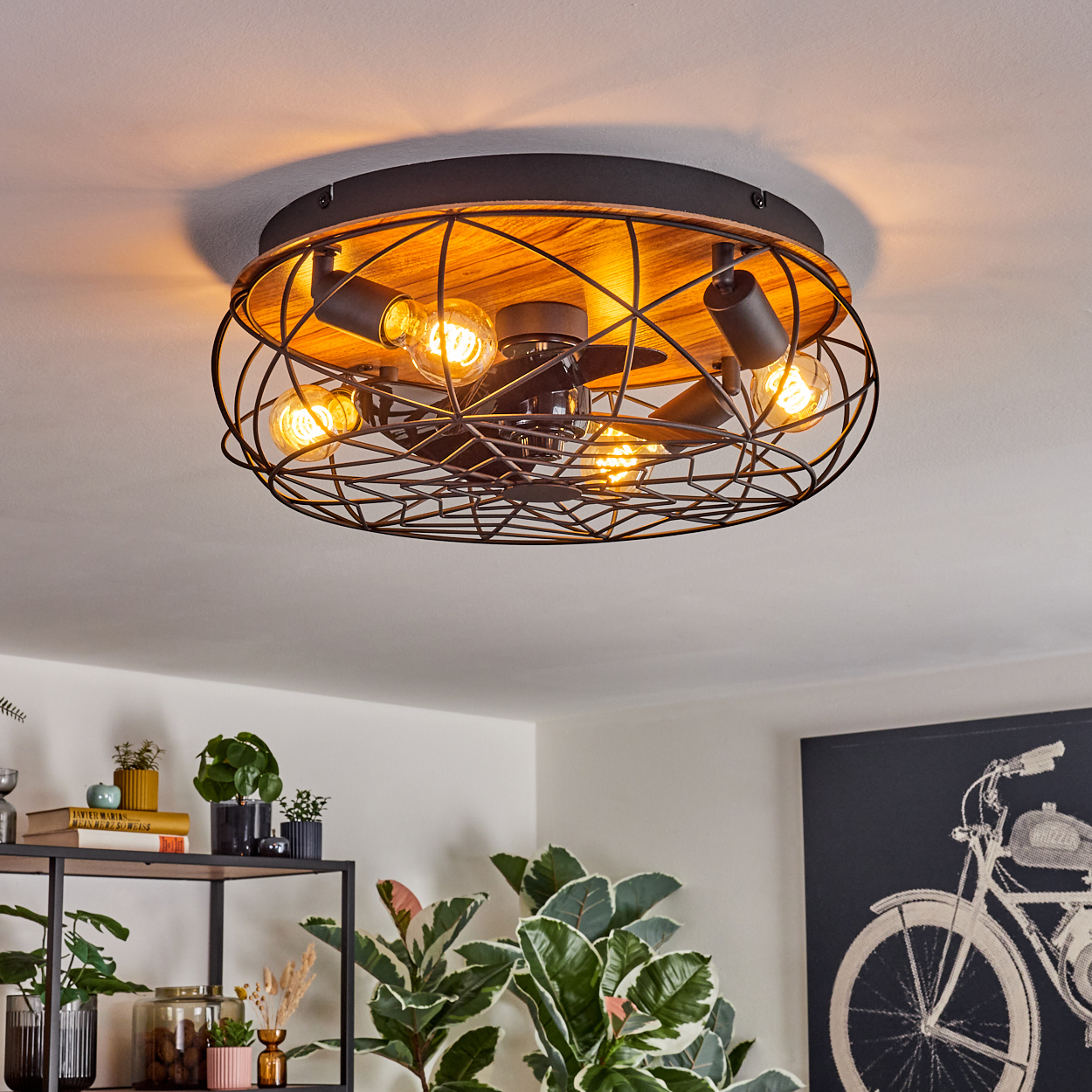 Deckenleuchte mit freiliegenden Glühbirnen und Holzsockel. Der Raum hat Pflanzen und ein Fahrradkunstwerk an der Wand.