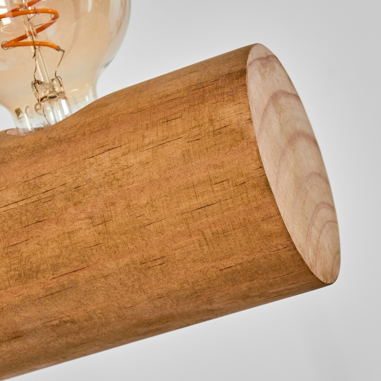 Nahaufnahme eines Holzbalkens mit einer Glühbirne im Hintergrund. Der Balken ist braun und die Glühbirne ist klar mit einem orangefarbenen Glühfaden.