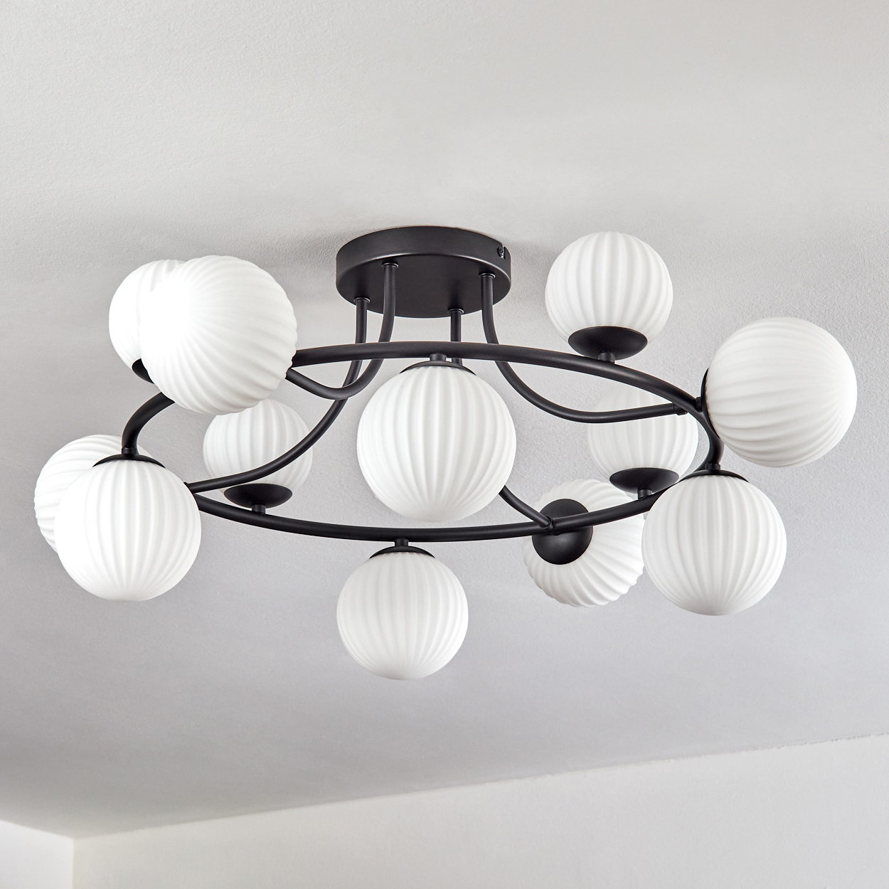 Eine moderne Deckenleuchte mit schwarzem Metallrahmen und zehn weißen, kugelförmigen Glasschirmen. Sie befindet sich an einer weißen Decke.