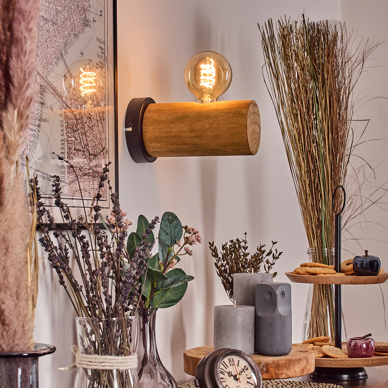 Holzlampe mit Glühbirne an der Wand, verschiedene Vasen, Kerzen und eine Eulenstatue auf einem Holztisch. Hintergrund ist eine Karte.