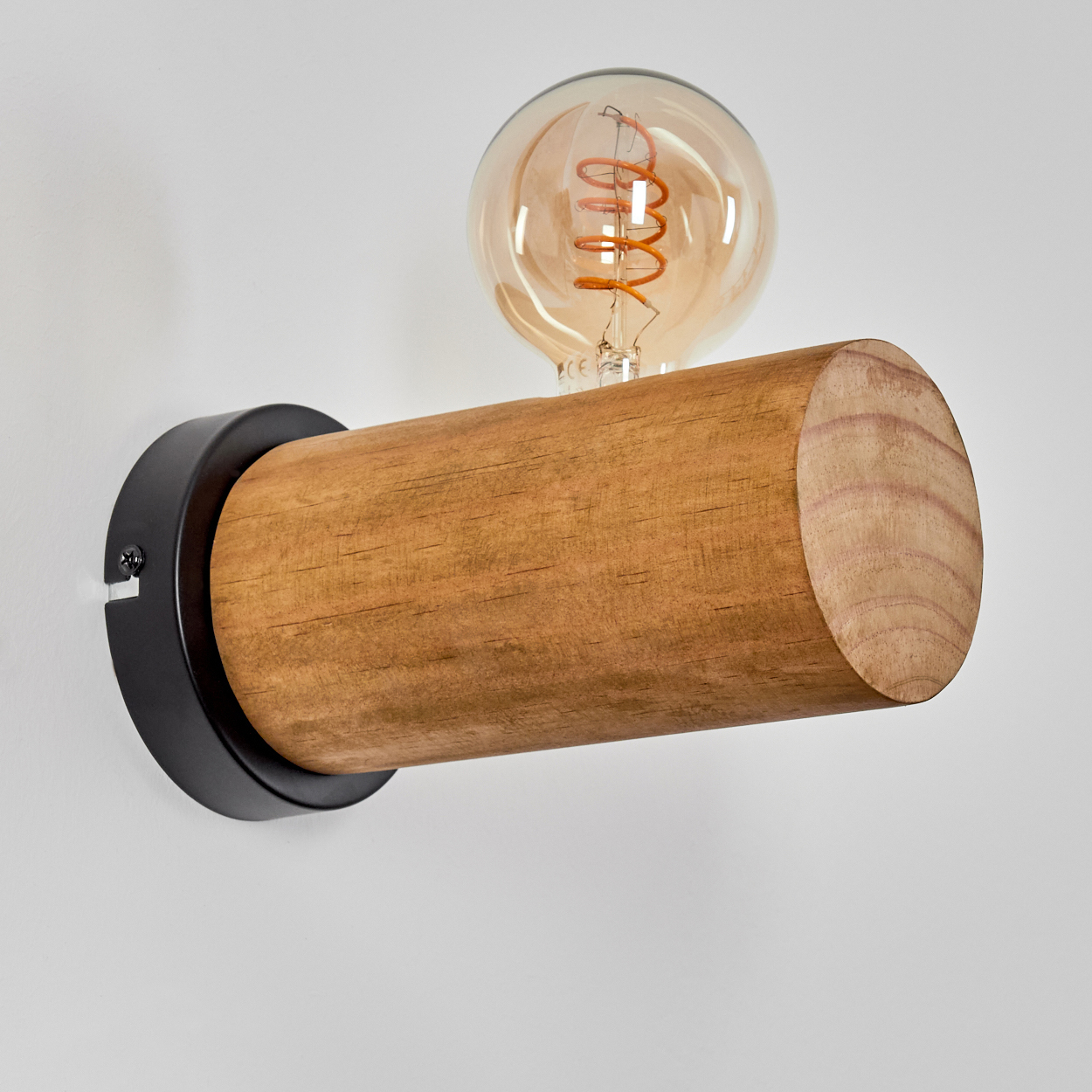 Eine hölzerne Wandleuchte mit einer runden, warm getönten Glühbirne an einer weißen Wand. Die Lampe hat einen zylindrischen Holzkörper und einen schwarzen Metallsockel.