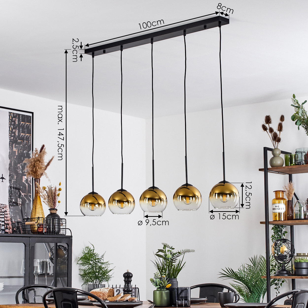 Ein modernes Esszimmer mit einer schwarzen und goldenen Pendelleuchte. Das Licht hat fünf Glaskugeln. Ein Esstisch und Dekorationsartikel sind ebenfalls sichtbar.