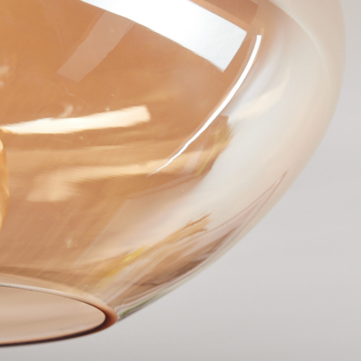 Nahaufnahme eines klaren Glasobjekts mit bernsteinfarbenem Farbton. Das Glas reflektiert Licht, der Hintergrund ist weiß.