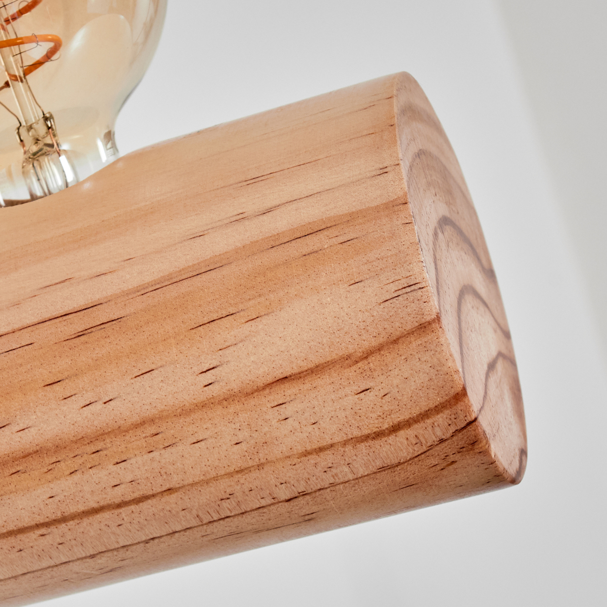 Nahaufnahme eines Holzbalkens mit sichtbarer Maserung. Eine Glühbirne ist teilweise auf der linken Seite vor weißem Hintergrund zu sehen.