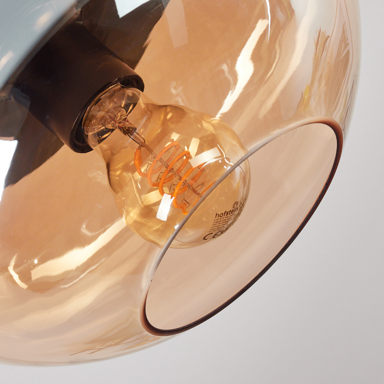 Nahaufnahme einer Leuchte mit braunem Glasschirm und warmtoniger Glühbirne. Der Hintergrund ist weiß.
