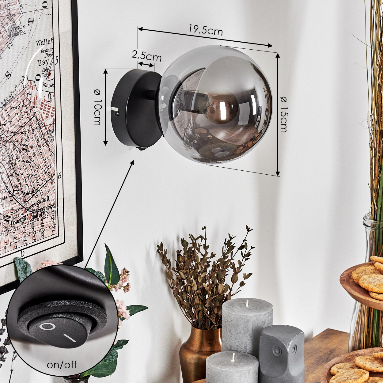 Eine Wandlampe mit kugelförmigem Schirm ist an einer weißen Wand befestigt. Die Lampe befindet sich in der Nähe einer gerahmten Karte, Kerzen und Snacks.