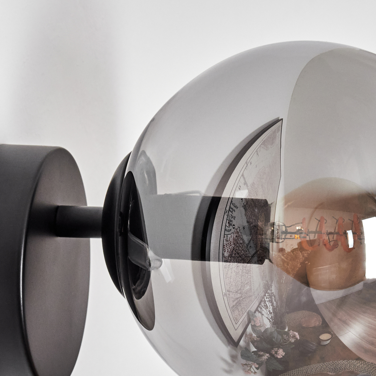 Eine moderne Wandlampe mit einem kugelförmigen Glasschirm. Im Inneren ist eine Karte zu sehen. Die Lampe ist auf einem schwarzen Metallsockel montiert.