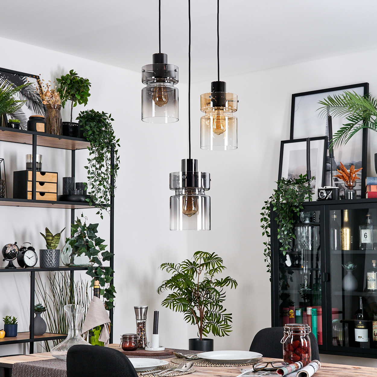 Esszimmer mit drei Hängelampen, Tisch gedeckt. Regale und Schrank mit Pflanzen und Dekoration.