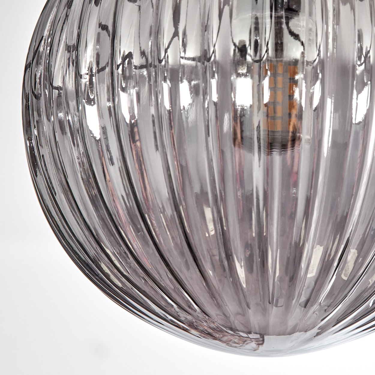 Nahaufnahme einer Glasleuchte, geripptes Design, transparent, reflektiert Licht, mit sichtbarer Glühbirne im Inneren.