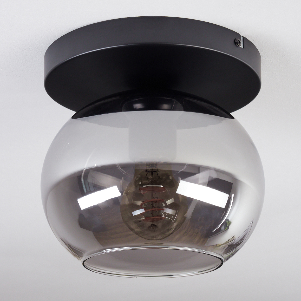 Eine moderne Deckenlampe mit schwarzem Sockel und kugelförmigem, rauchfarbenem Glasschirm, der eine sichtbare Glühbirne zeigt.