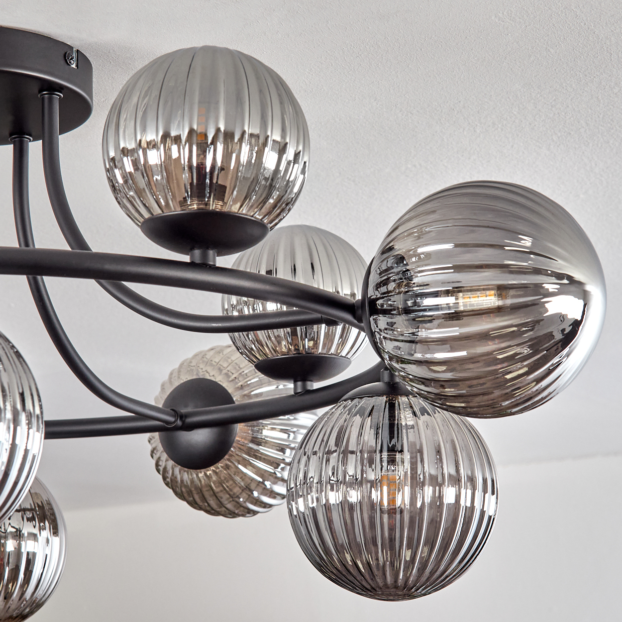 Eine moderne Deckenleuchte mit mehreren gerippten Glaskugeln an schwarzen Metallarmen. Der Hintergrund ist eine weiße Decke.