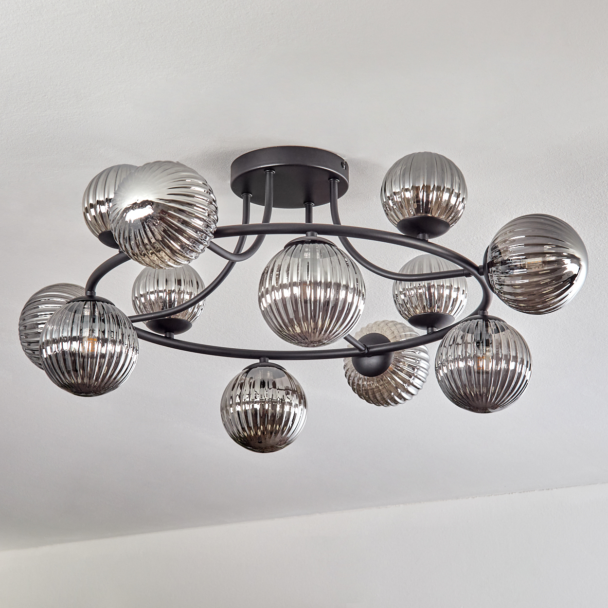 Eine moderne Deckenleuchte mit mehreren silbernen, gerippten Glaskugeln in kreisförmiger Anordnung, an einer weißen Decke montiert.