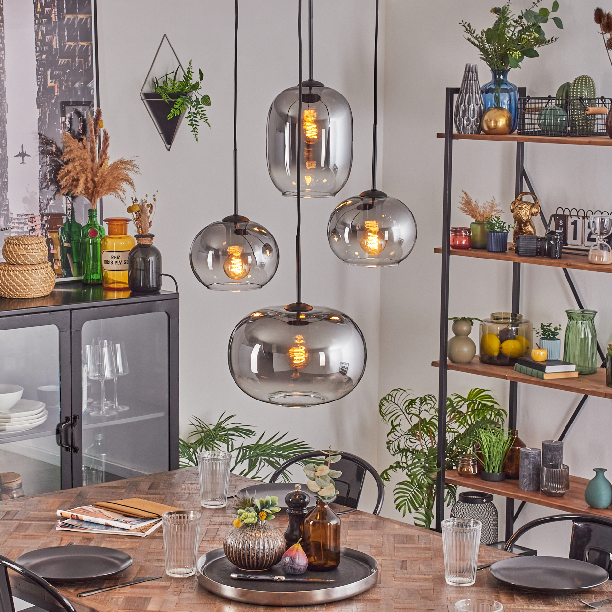 Esszimmer mit Hängelampen, Tisch mit Tellern, Gläsern und Dekoration sowie ein Regal mit verschiedenen Dekorationsartikeln.