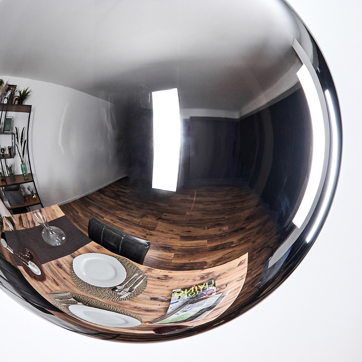 Ein Fischaugenblick reflektiert einen Essbereich. Ein Tisch ist mit Tellern, Besteck und einer Zeitschrift gedeckt. Der Raum hat Holzböden und einen schwarzen Stuhl.