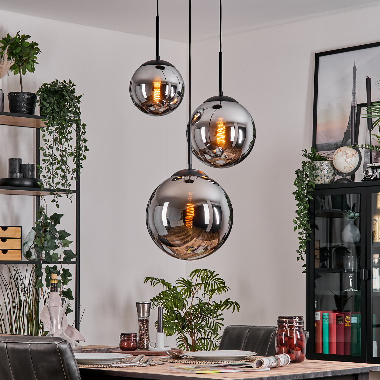 Drei kugelförmige Lampen hängen über einem Esstisch. Im Hintergrund sind Regale und ein Schrank zu sehen.