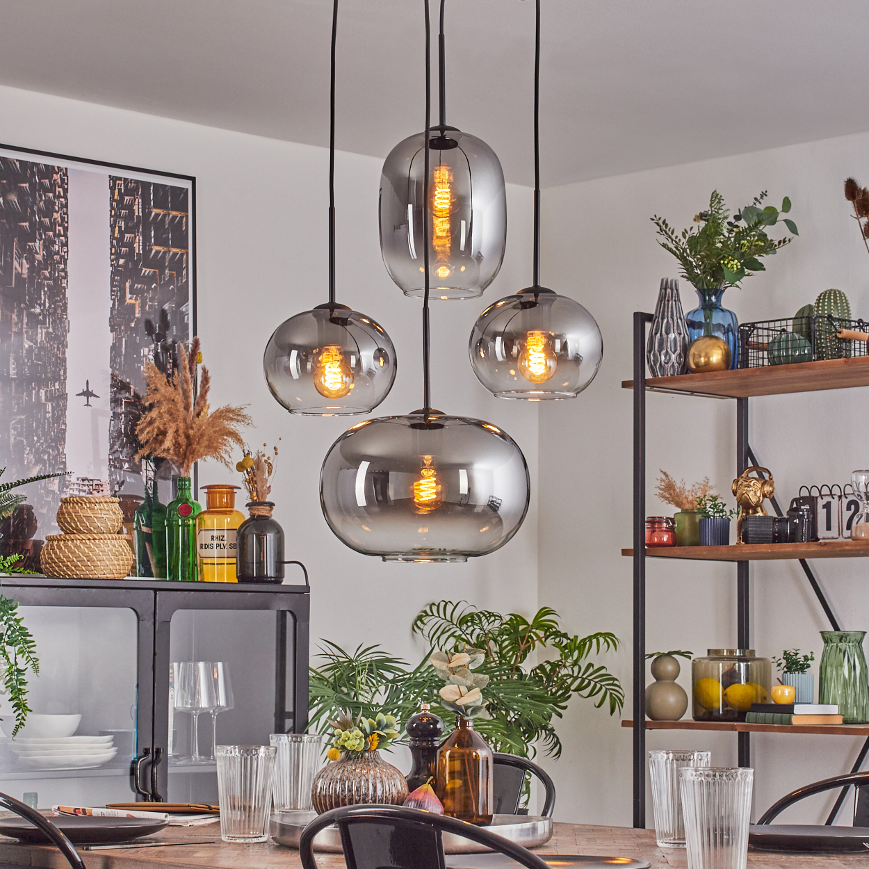 Esszimmer mit Hängelampen, gedecktem Tisch. Regale mit Dekoration rechts. Pflanzen, Gläser und ein Schrank sind sichtbar.