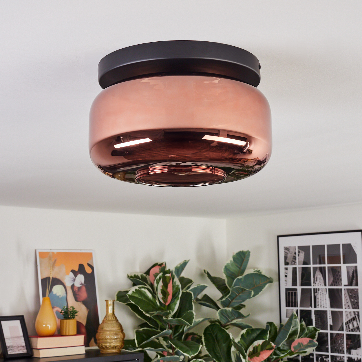 Eine moderne, kupferfarbene Deckenleuchte ist installiert. Der Raum hat Pflanzen und Kunstwerke. Die Decke ist weiß.