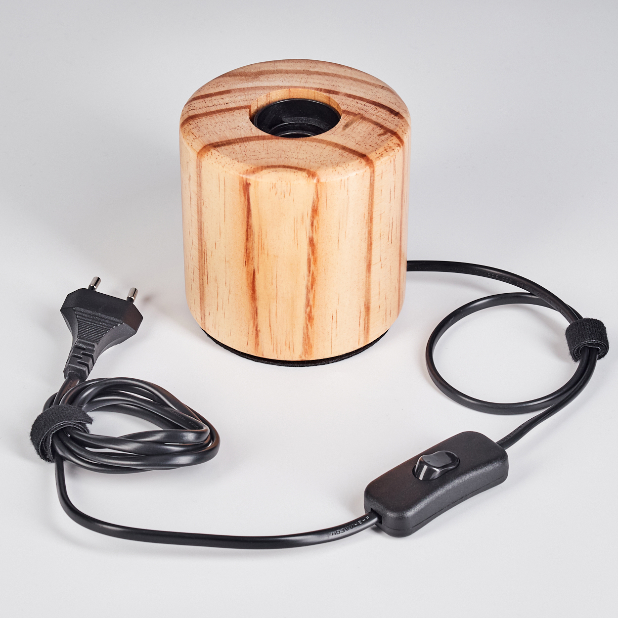 Eine hölzerne Zylinderlampe mit schwarzem Kabel, Schalter und Stecker auf weißem Untergrund. Die Lampe hat ein Loch oben.