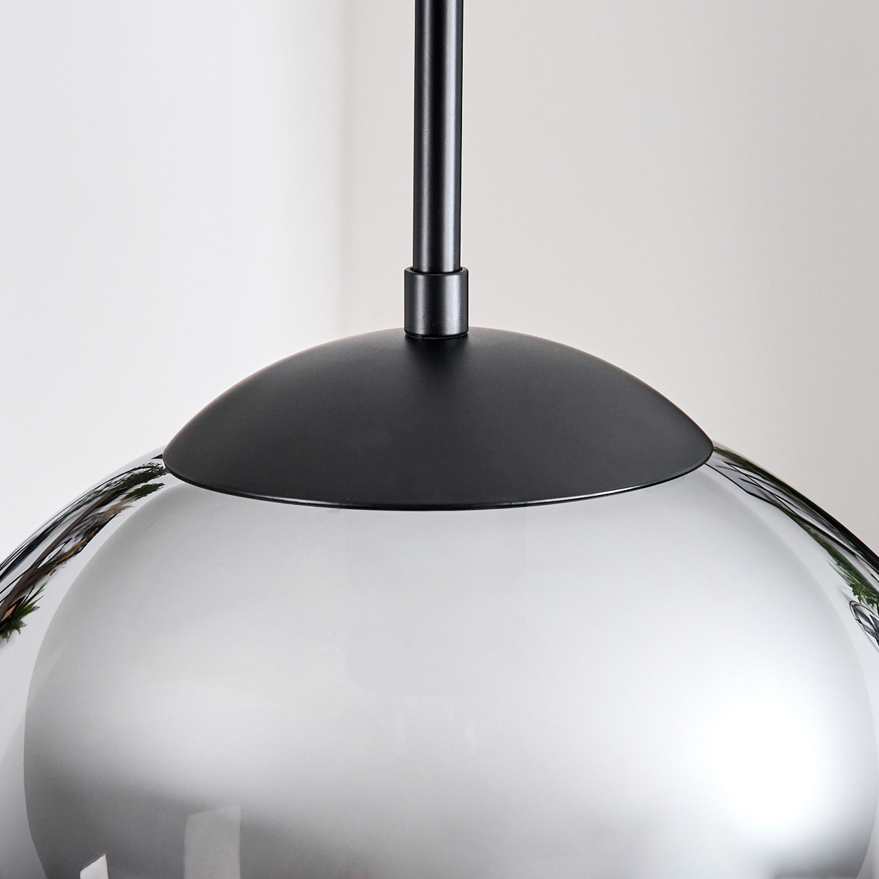 Eine moderne Pendelleuchte mit schwarzer Kappe und Stiel sowie einem reflektierenden, silbern gefärbten Glasschirm auf weißem Hintergrund.
