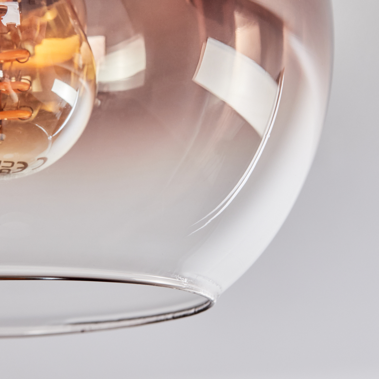 Nahaufnahme einer Glasleuchte. Ein klarer Glasschirm umgibt eine Glühbirne und reflektiert das Licht. Der Hintergrund ist weiß.