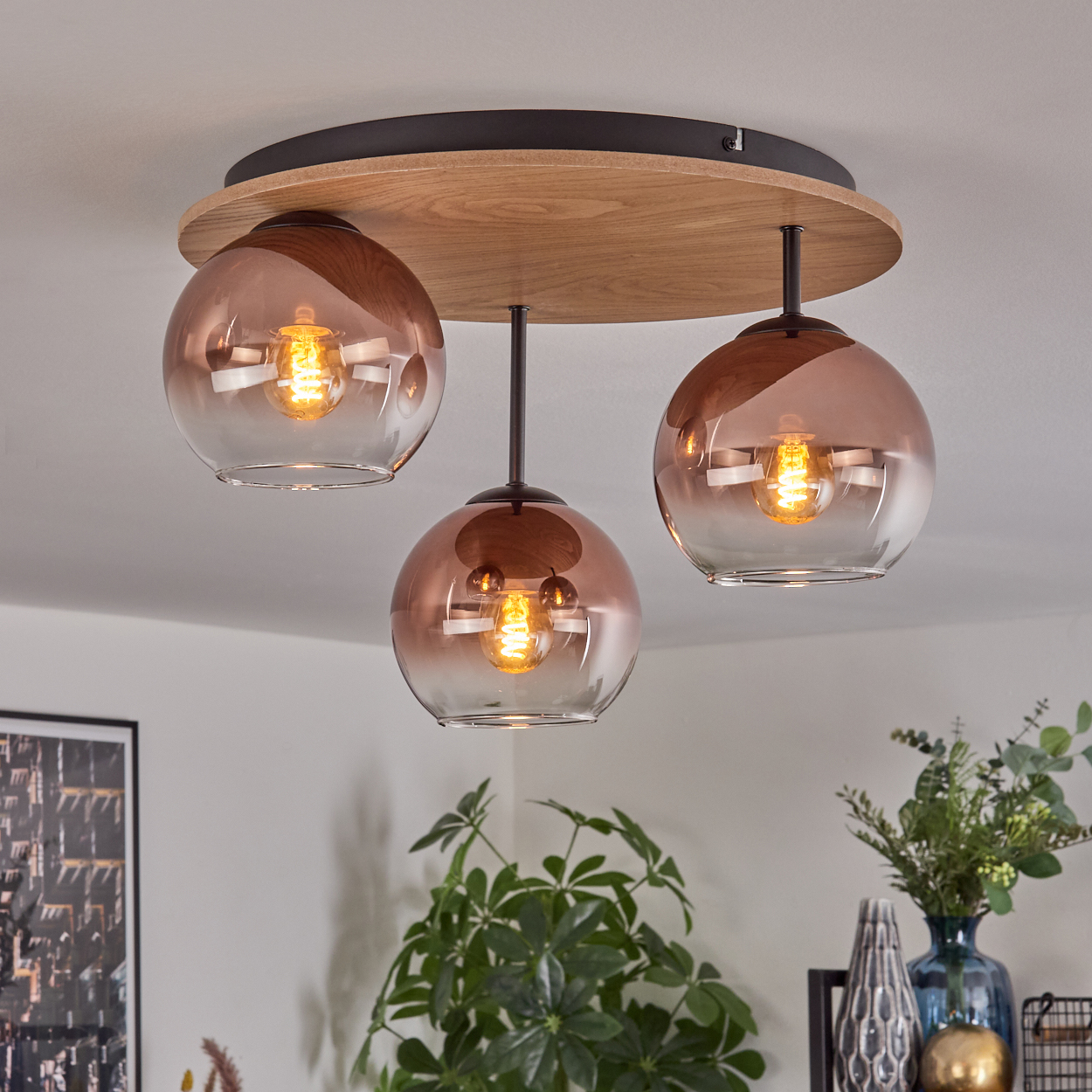 Eine Deckenleuchte mit drei Glaskugelschirmen, jede mit warmem Licht. Die Leuchte hat einen Holzsockel.