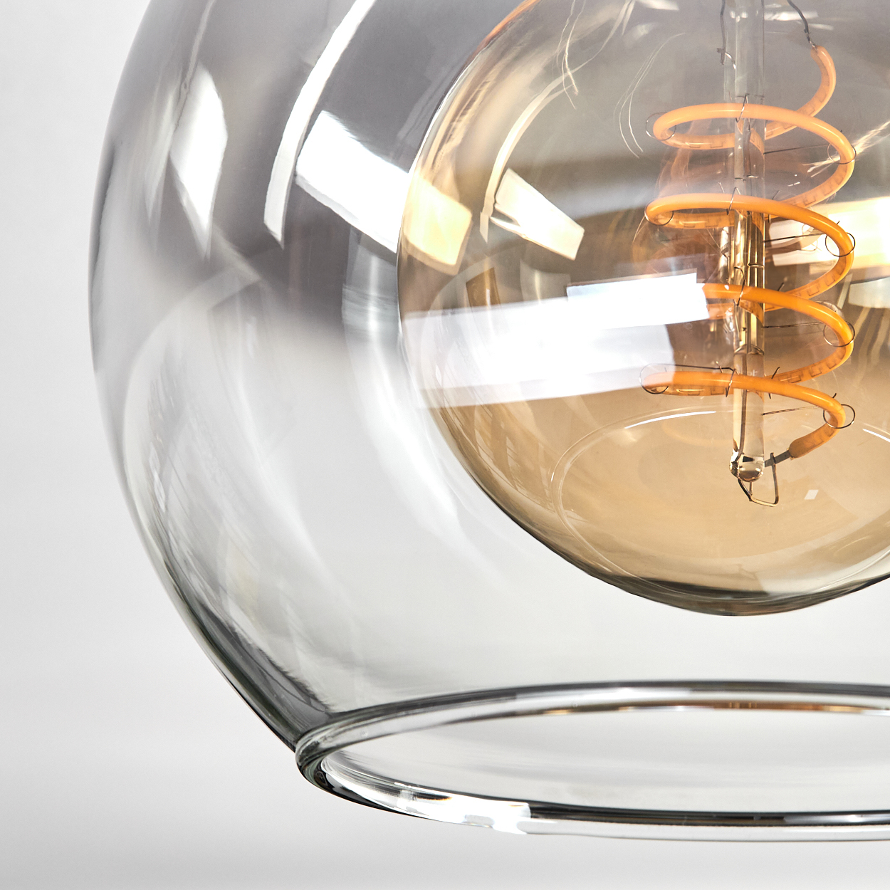 Nahaufnahme einer Glasleuchte. Im Inneren glüht ein Spiralfilament. Das Glas ist klar mit einer reflektierenden Oberfläche.
