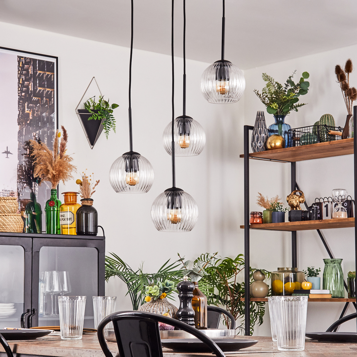 Esszimmer mit Hängelampen, Glasvasen, Pflanzen und einem Holztisch, der für eine Mahlzeit gedeckt ist. Regale mit Dekoration sind ebenfalls vorhanden.