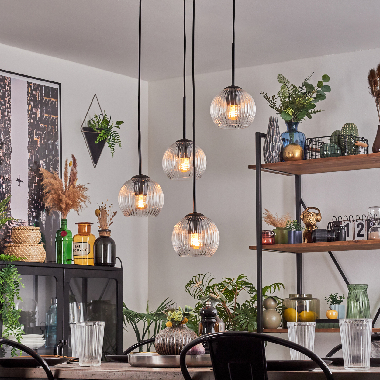 Esszimmer mit hängenden Kugelleuchten. Tisch mit Gläsern gedeckt. Regale mit Deko. Pflanzen, Kunstwerke und verschiedene Dekorationsartikel.
