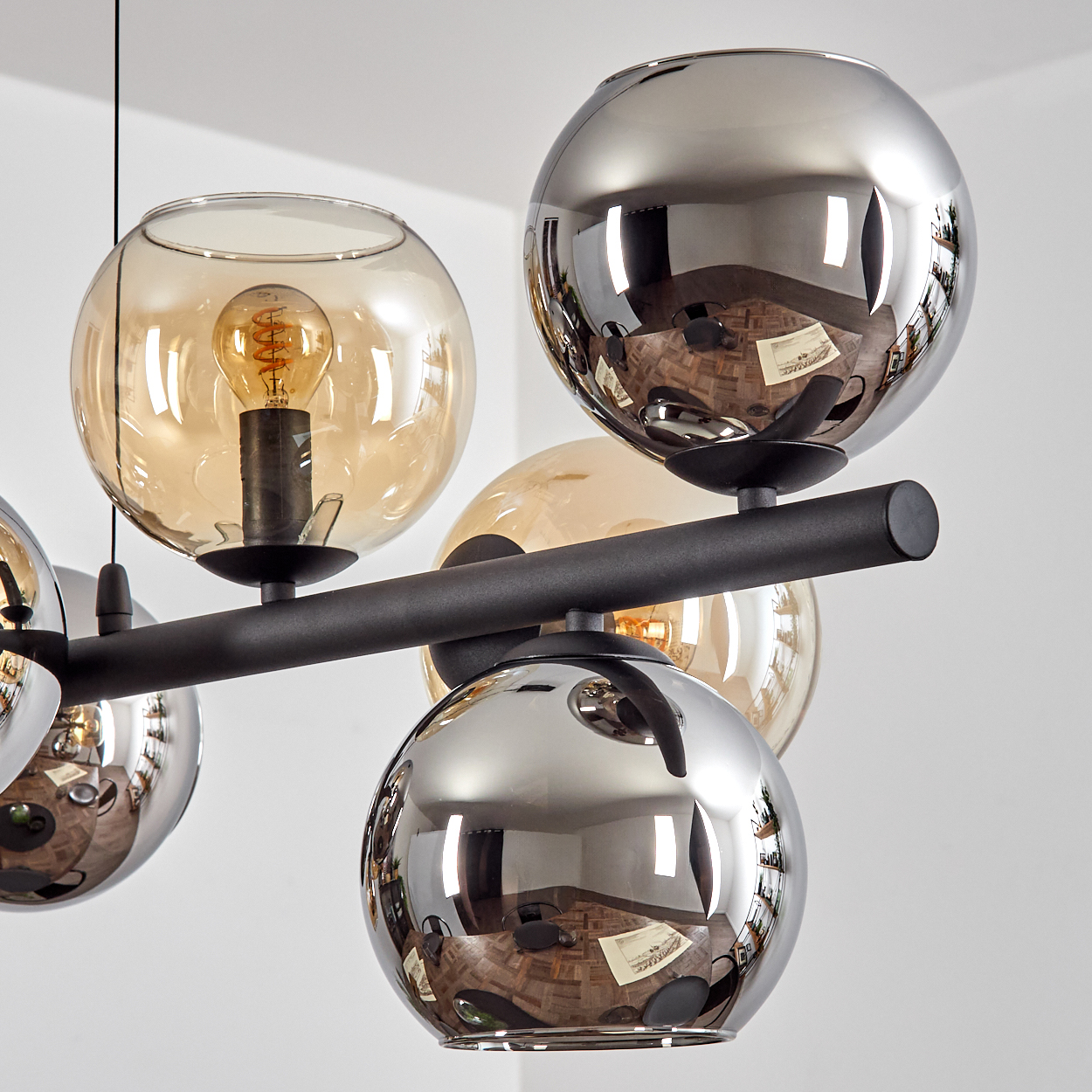 Eine moderne Deckenleuchte mit mehreren kugelförmigen Glasschirmen. Einige sind klar, andere verspiegelt. In einigen Schirmen ist eine Glühbirne.