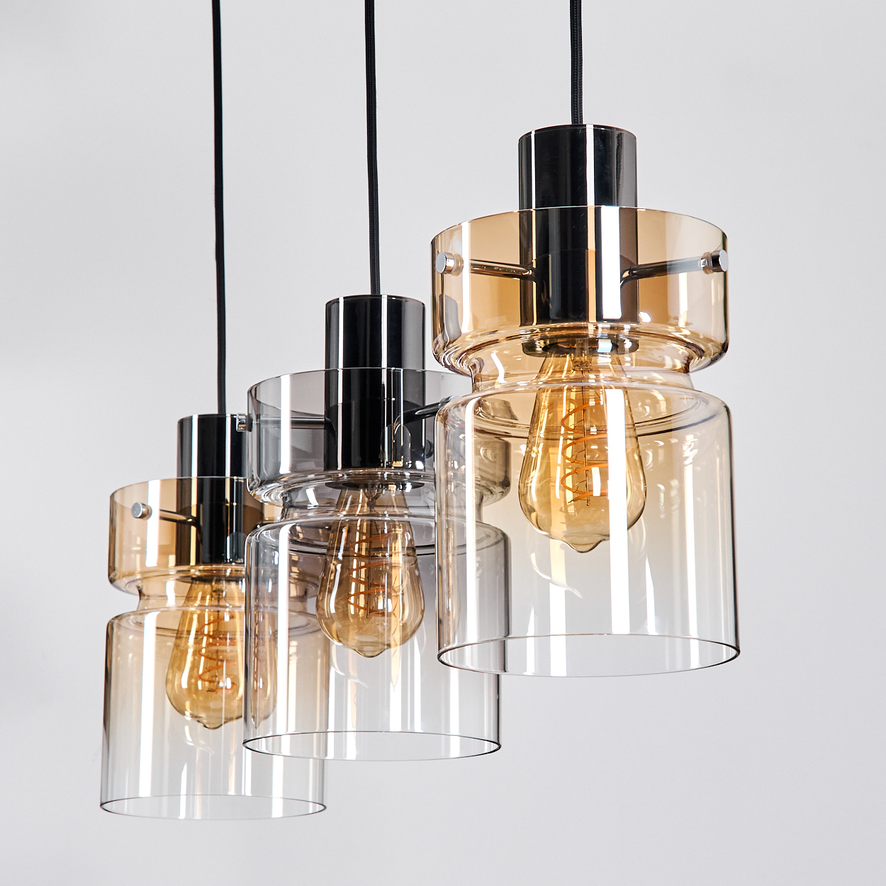 Drei Pendelleuchten mit Glasschirmen und Edison-Glühbirnen hängen vor weißem Hintergrund. Die Schirme sind bernsteinfarben und klar.
